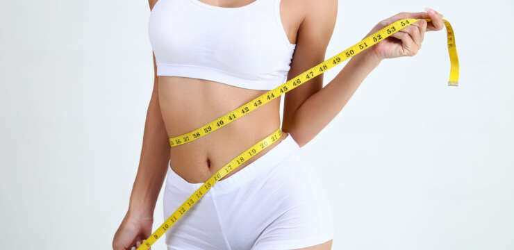 Close up slimming female with beautiful body and measuring her waistline with measure tape on white background and copy space